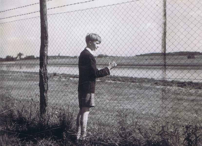 Eine Schwarz-Weiß-Aufnahme eines Jungen, der an einem Drahtzaun steht und in die Ferne blickt
