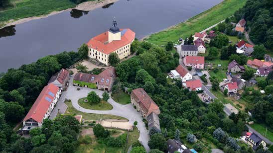 Luftaufnahme eines Schlosses und seiner Umgebung, im Hintergrund ist ein Fluß zu sehen