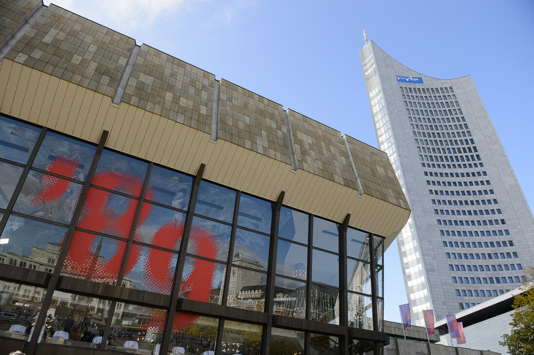 Die Glasfassade eines Gebäudes, auf der »´89« steht. Im Hintergrund ist ein Hochhaus zu sehen.