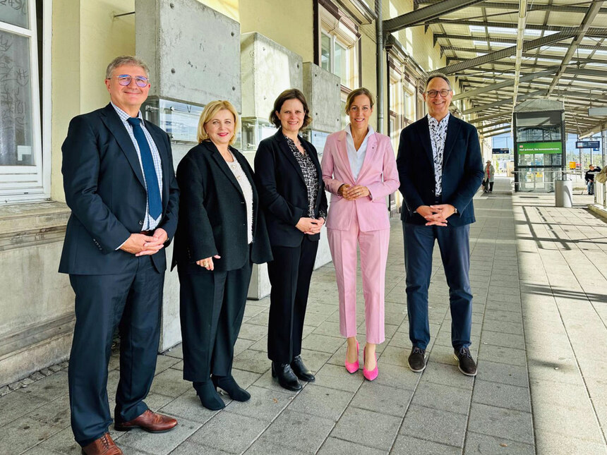 Männer und Frauen stehen an einem Bahngleis.