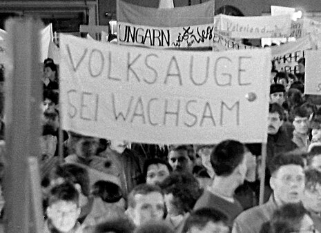 Ein Demonstrartionszug mit einem Plakat auf dem geschrieben steht: Volksauge sei wachsam.