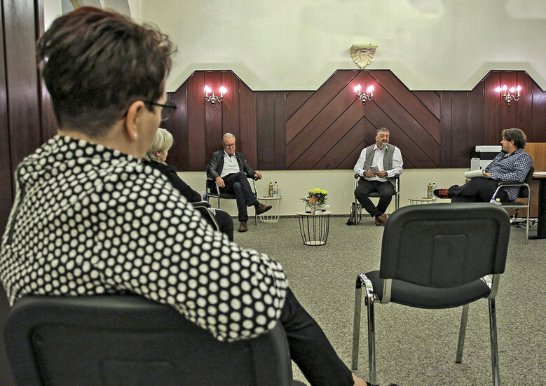 Männer und Frauen sitzen in einem Saal und unterhalten sich.