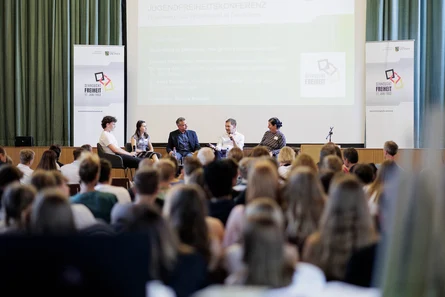 Männer und Frauen diskutieren vor Publikum auf einer Bühne.