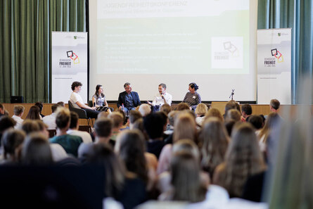 Männer und Frauen diskutieren vor Publikum auf einer Bühne.
