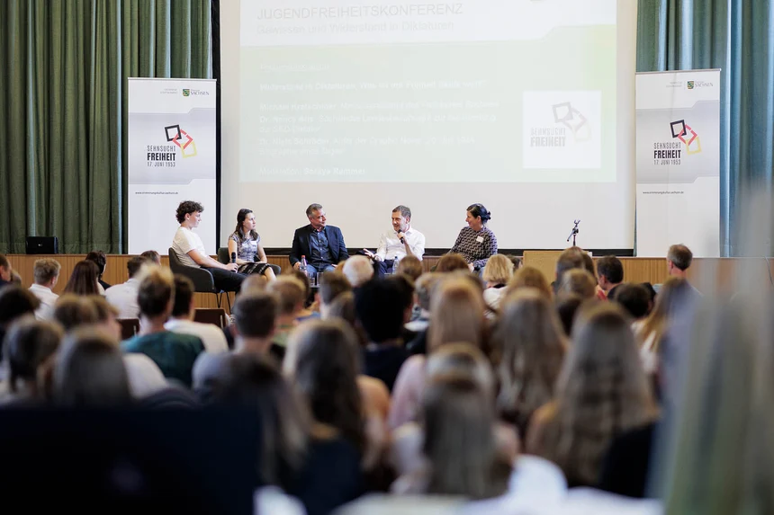 Männer und Frauen diskutieren vor Publikum auf einer Bühne.