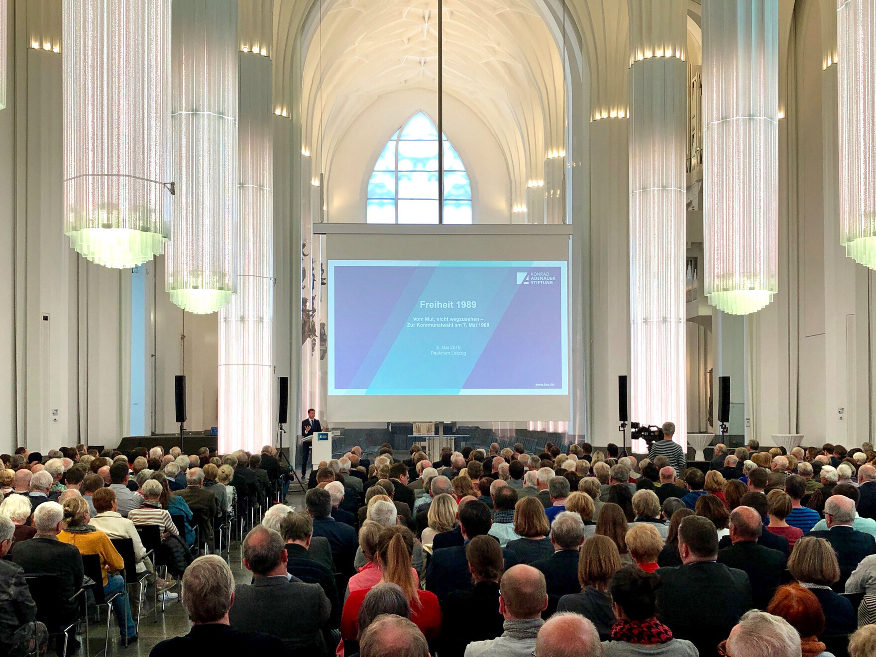 Ein großer Saal in dem viele Menschen sitzen.