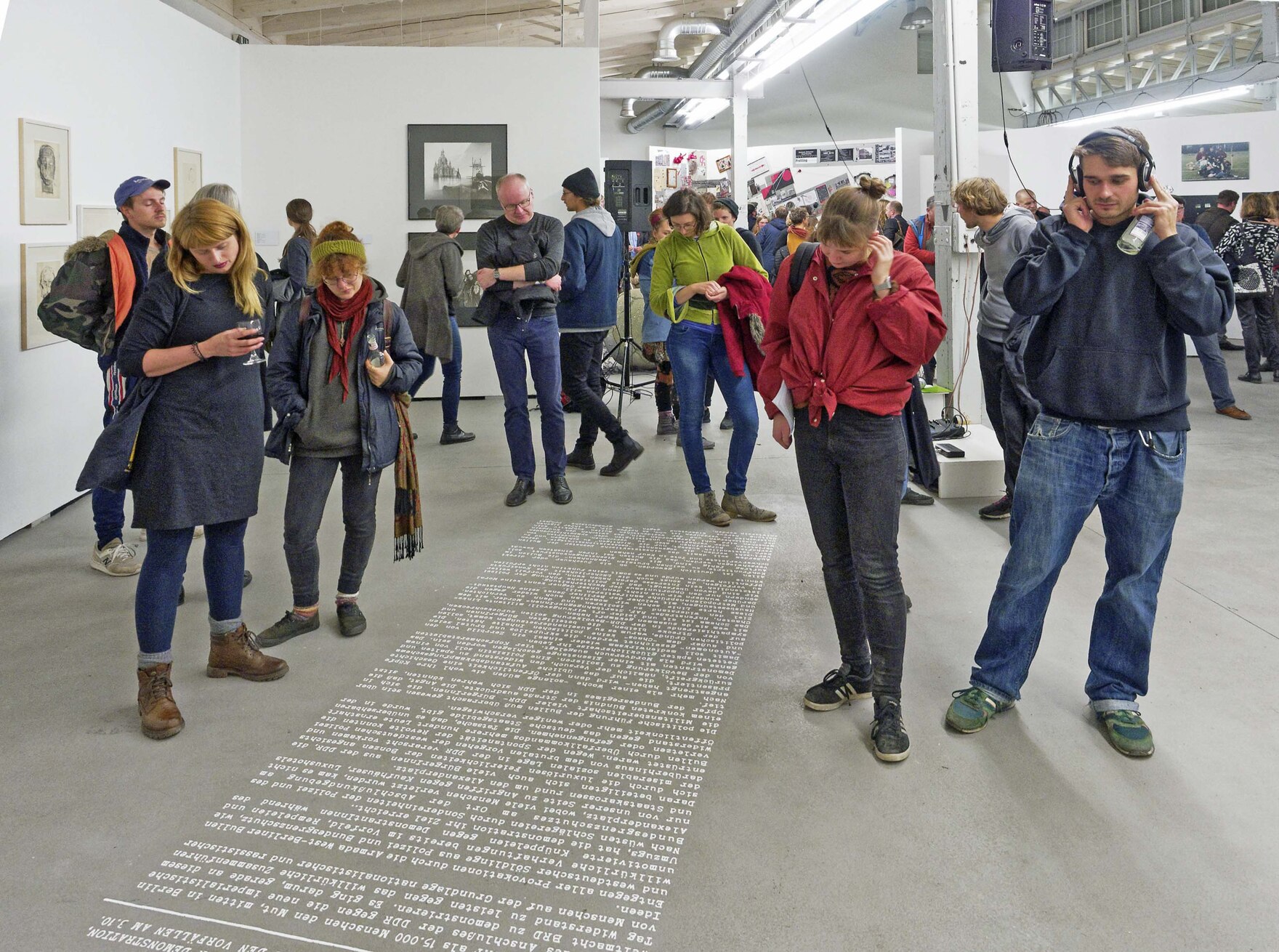 Männer und Frauen stehen in einer Halle und blicken auf den Fußboden.